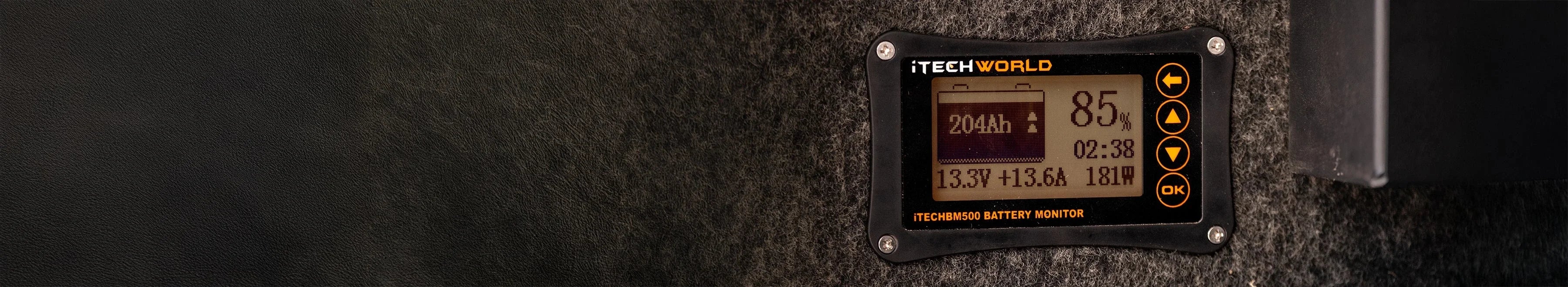 Close-up of a TECHWORLD battery monitor displaying voltage, amperage, and time data on a digital screen, mounted on a textured surface with leather and dark material visible.