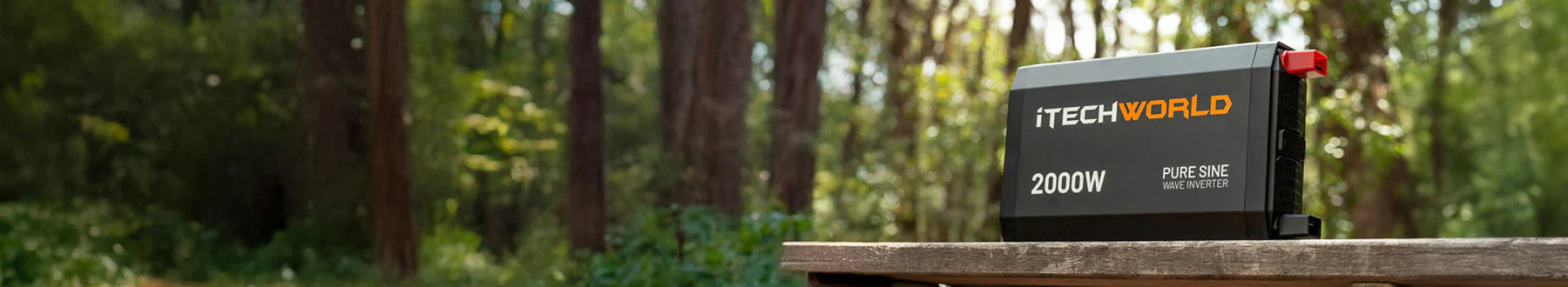 A black iTechworld 2000W pure sine wave inverter sits on a wooden surface outdoors, with a blurred forest background of tall trees and sunlight.