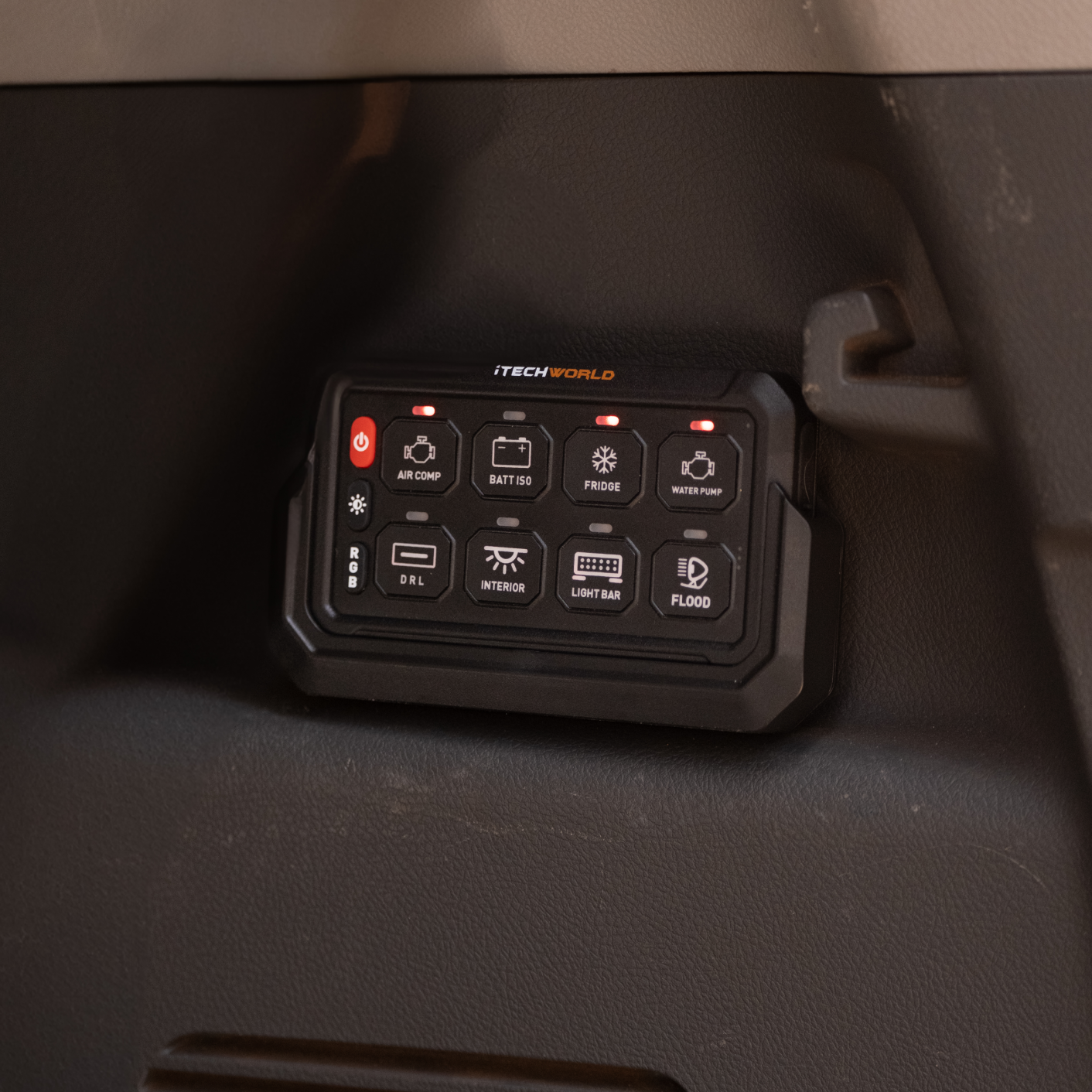 An iTechworld 8 Gang Wireless Switch Panel is mounted on a vehicle dashboard, with labeled buttons for air compressor, lights, fridge, water pump, and other 12V accessories; some indicator lights are illuminated.