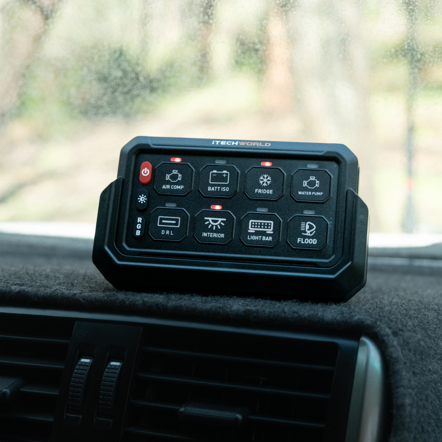 An iTechworld 8 GANG Wireless Switch Panel with labeled buttons rests on a car dashboard, with a foggy windshield and trees outside, showcasing iTechworlds convenient control of 12V accessories while driving.
