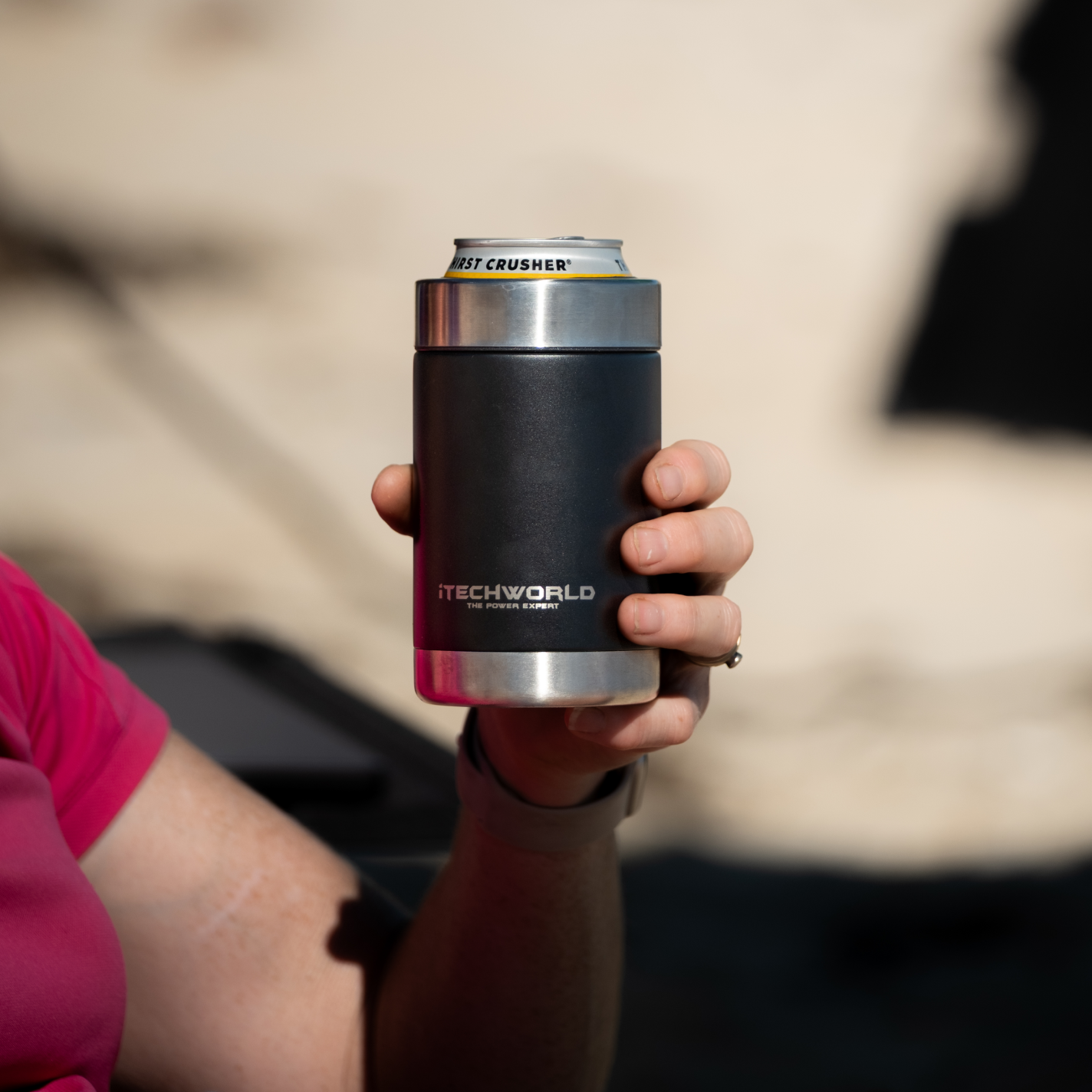 A person in a pink shirt holds an iTechworld | Can Cooler | 375mL with a can inside, set against a blurred, sunlit background that highlights the sleek stainless steel design.