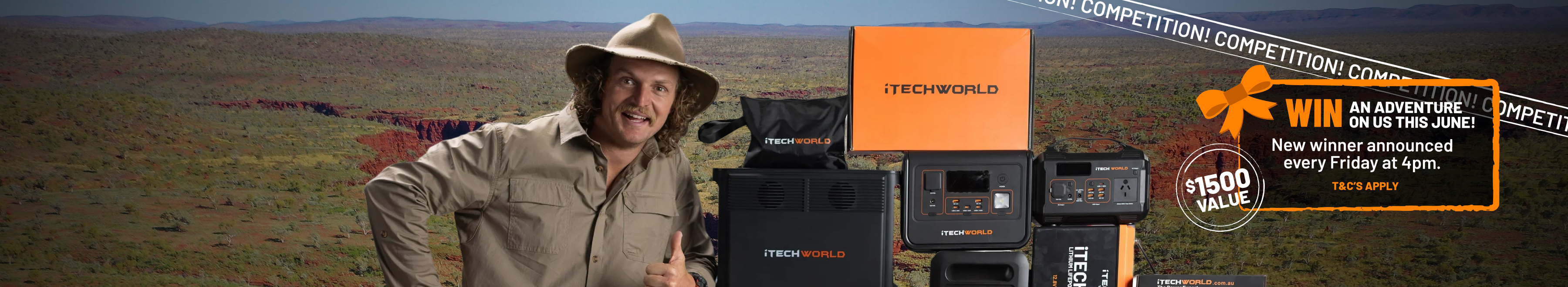 A man in a khaki shirt and hat smiles while standing beside a stack of Tech World branded power equipment and boxes, in a workshop setting.