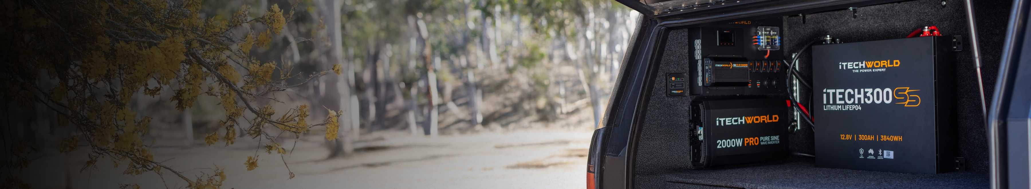 A person holds a large battery labeled “TECH120” while installing it into the engine compartment of a white vehicle outdoors at sunset.