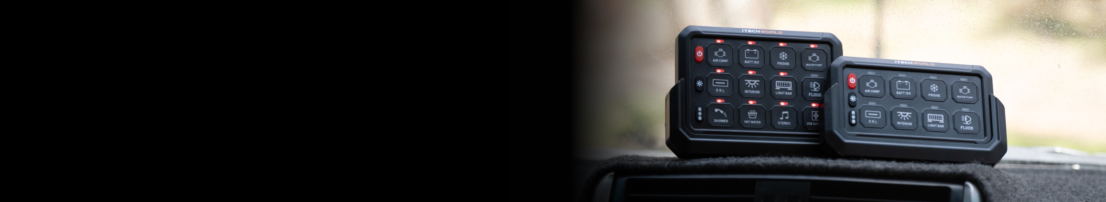Two black electronic control panels with illuminated buttons sit on a car dashboard. The background is blurred, with the left side of the image mostly black.