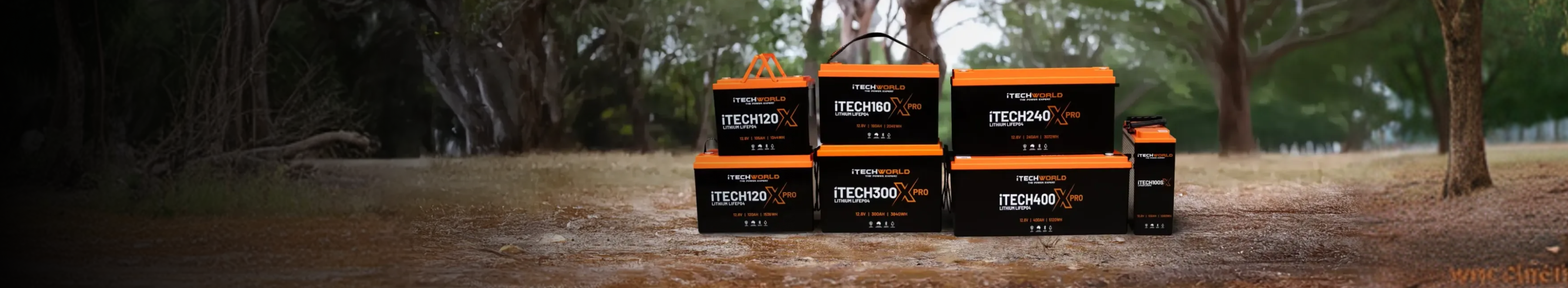 Four TrekN Solar batteries are stacked on a large rock with green trees and hills in the background under a clear blue sky.