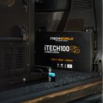An iTechworld | Mini Power Core + Super Slim 100Ah battery in black sits inside a vehicle near the rear door, partially on a carpeted surface, with interior panels of the vehicle visible in the background.