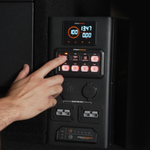 A hand presses a button on the black iTechworld | Mini Power Core + Super Slim 100Ah control panel, featuring illuminated switches, digital displays, and power outlets.