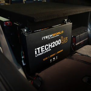 An iTechworld iTECH200US Ultra Slim 200Ah 12V LiFePO4 Bluetooth battery is installed behind the vehicle's rear seat, partially under a raised platform, with technical specs and branding visible on its side.