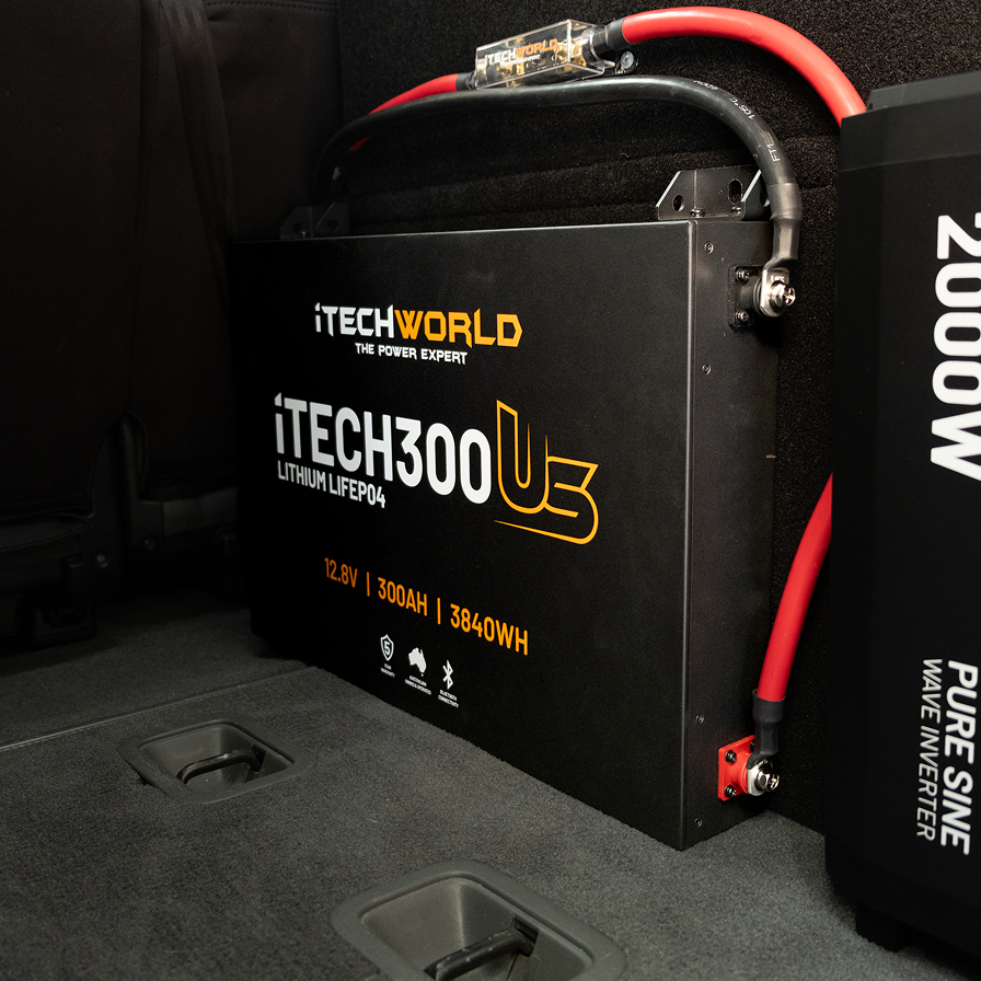An iTechworld iTECH300US Ultra Slim Deep Cycle LiFePO4 12.8V 300Ah battery with Bluetooth is installed in a vehicle, featuring red and black cables (3840Wh). A 2000W Pure Sine Wave Inverter is partially visible nearby.