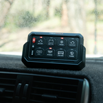 An iTechworld 8 GANG Wireless Switch Panel with labeled buttons rests on a car dashboard, with a foggy windshield and trees outside, showcasing iTechworlds convenient control of 12V accessories while driving.