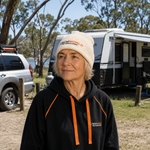 A woman wearing the iTechworld Cream Beanie stands outdoors by a camper and car, enjoying a peaceful moment in nature with trees and a lake in the background.
