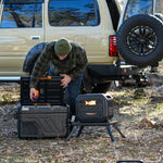 An individual dressed in outdoor apparel places an apple into a portable fridge beside the iTechworld 2800W 180AH PS2800 PRO Portable Lithium Power Station with Bluetooth, while an SUV with an open rear hatch is visible among trees and leaves in the background.