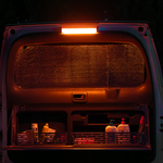 The open back door of a van is lit by an iTechworld Magnetic LED Strip Light (300LM), revealing two shelves with bottles of lotion, paper cups, a spray bottle, and napkins. A metallic screen covers the window.