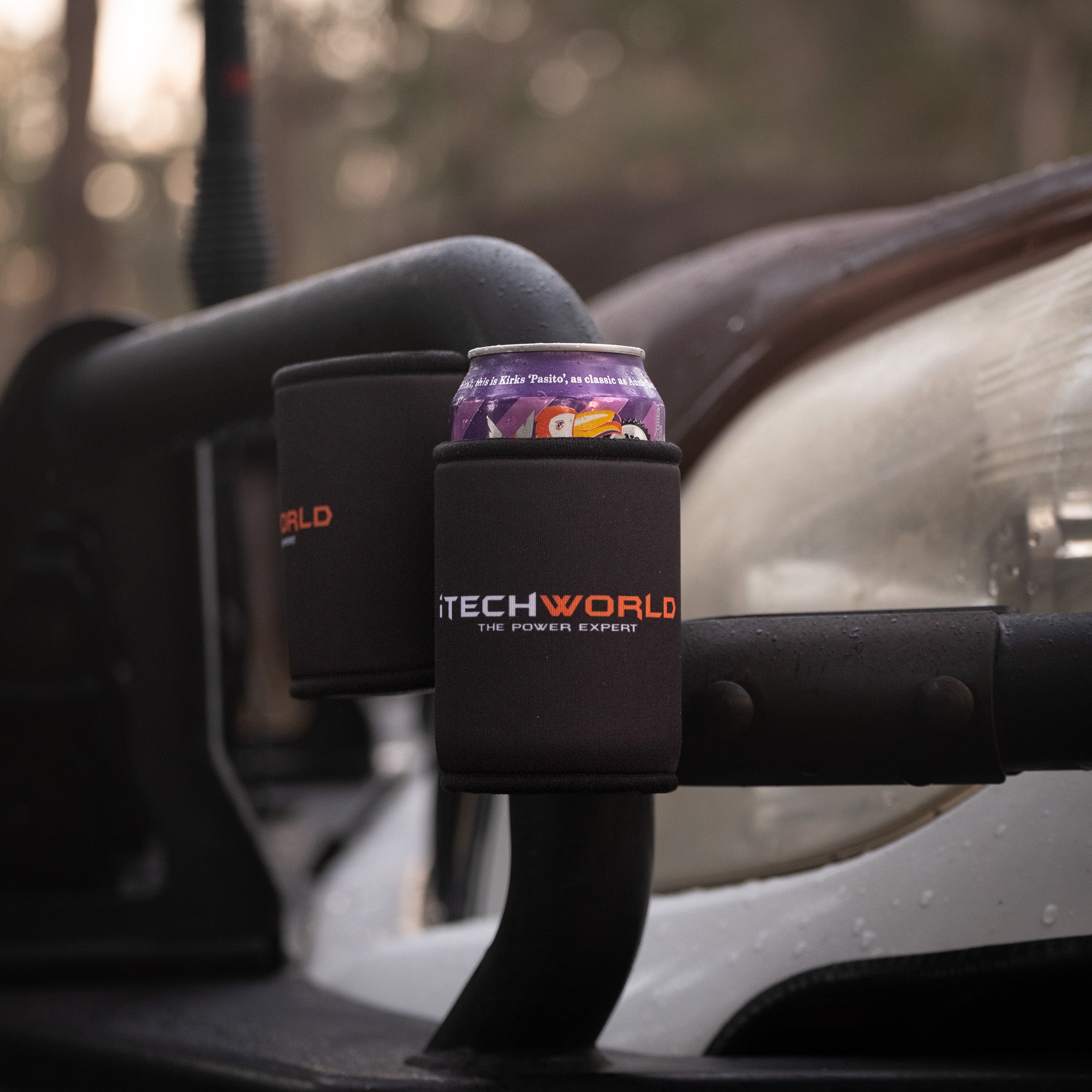 A purple soda can is held in an iTechworld Magnetic Stubby Holder (375mL), attached to a vehicle’s metal frame with outdoor scenery blurred in the background.