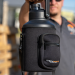A person holds a large black iTechworld | 3.8L Water Bottle with a handle, encased in a zippered neoprene sleeve with two compartments and the iTechworld logo. The sunlit outdoor background is softly blurred.