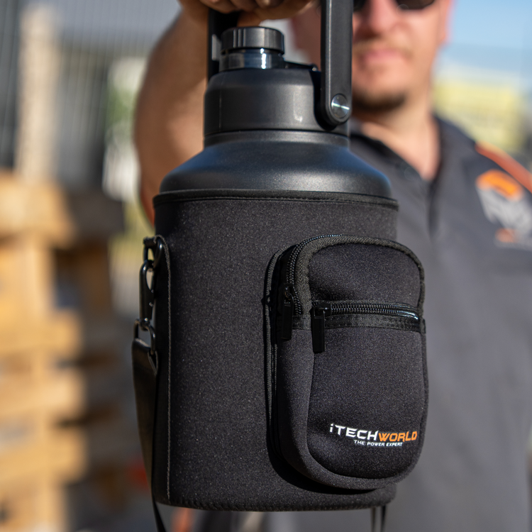 A person holds a large black iTechworld | 3.8L Water Bottle with a handle, encased in a zippered neoprene sleeve with two compartments and the iTechworld logo. The sunlit outdoor background is softly blurred.