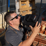 A man in sunglasses and a grey shirt drinks from an iTechworld 3.8L Water Bottle while sitting on bricks at a construction site.