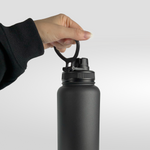 A person in a black sleeve holds the iTechworld 1.2L Water Bottle by its looped lid, showcasing its sleek, double-wall vacuum design and leak-proof hydration against a plain, light gray background.