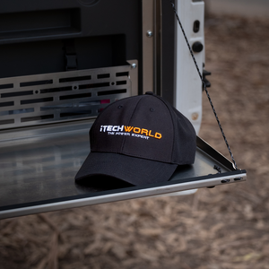The iTechworld Hat | Embroidered features “THE POWER EXPERT” in white and orange on black breathable cotton. This iTechworld cap provides sun protection, shown outdoors on metal with soil and dried leaves in the background.