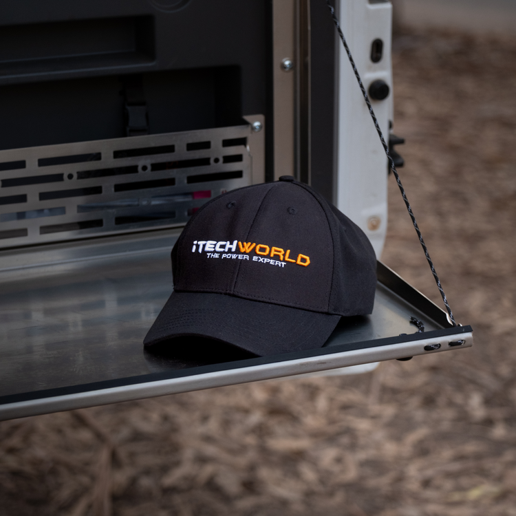 The iTechworld Hat | Embroidered features “THE POWER EXPERT” in white and orange on black breathable cotton. This iTechworld cap provides sun protection, shown outdoors on metal with soil and dried leaves in the background.