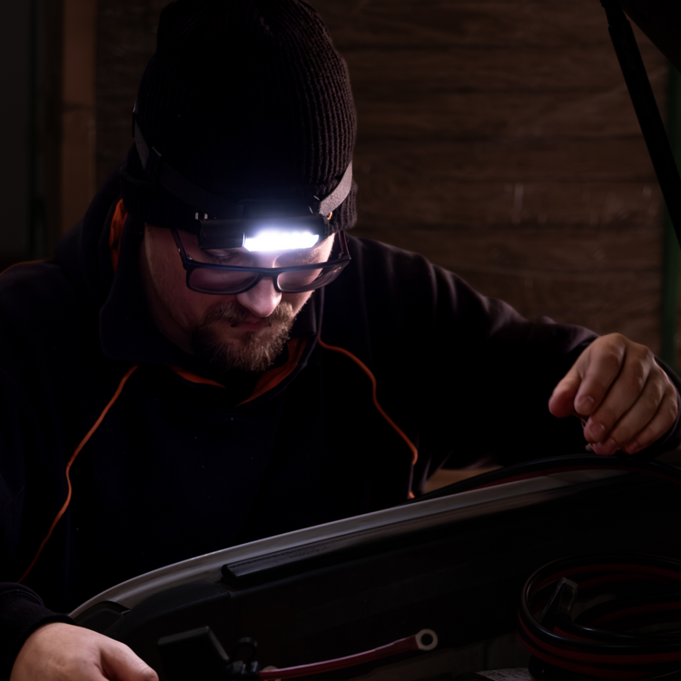 A man in glasses and a black beanie uses the iTechworld Magnetic Head Torch (450LM) to work under a car hood at night, illuminated by its ultra bright light.