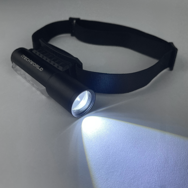 A black iTechworld Magnetic Head Torch (450LM) with an adjustable strap shines a bright beam on a white surface, making this rechargeable flashlight perfect as a camping light or head torch for any adventure.