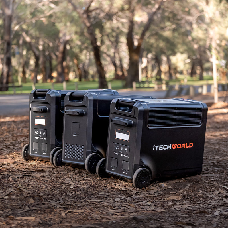 Three iTechworld PS3600 PRO Portable Lithium Power Stations (3600W 300Ah) rest on park ground among trees and leaves, sunlight streaming through. Each offers advanced LiFePO4 technology for dependable outdoor power.