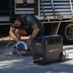 Wearing safety gear, a person uses a circular saw on wood, powered by an iTechworld 3600W 320Ah PS3600 PRO Portable Lithium Power Station with Bluetooth. In the background, a truck with an open cargo area waits for loading.