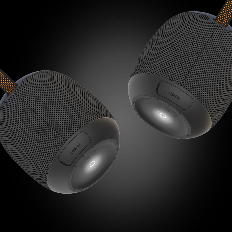 Two iTechworld Pulse Mini waterproof portable speakers, black and cylindrical with mesh exteriors, hang against a dark gradient backdrop. Each features a USB-IN port, power button at the base, and a fabric cord for easy portability.
