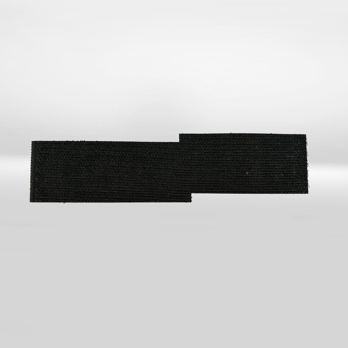 An iTechworld Velcro Patch, a rectangular black hook-and-loop fastener from iTechworld, lies on a plain white surface with a small section extending out on the right side.