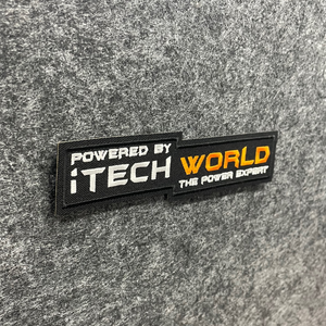 A rectangular iTechworld Velcro Patch displays the text: POWERED BY iTECH WORLD THE POWER EXPERT on gray fabric. The words “iTECH” and “WORLD” stand out in white and orange, forming a bold Power Expert logo embroidered by the iTechworld brand.