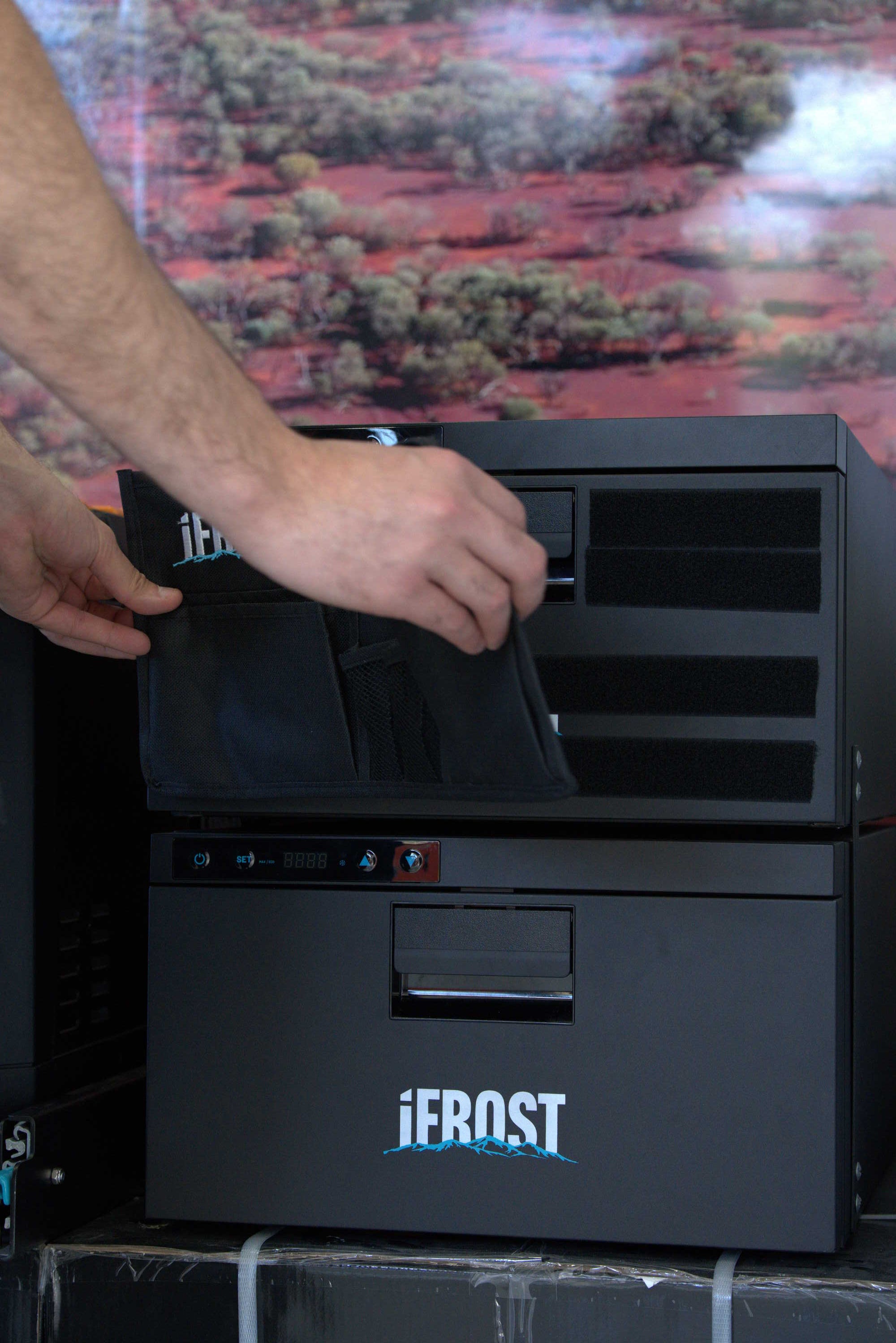 A person's hands are shown placing a black fabric pouch or organizer into the open compartment of a black Jerust branded cooler or storage unit.