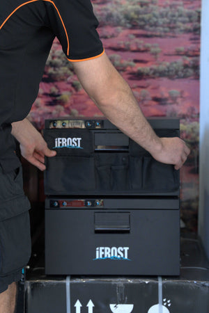 A person wearing a black shirt with orange trim is handling a black Jerost cooler or storage unit with multiple front compartments and visible Jerost branding.