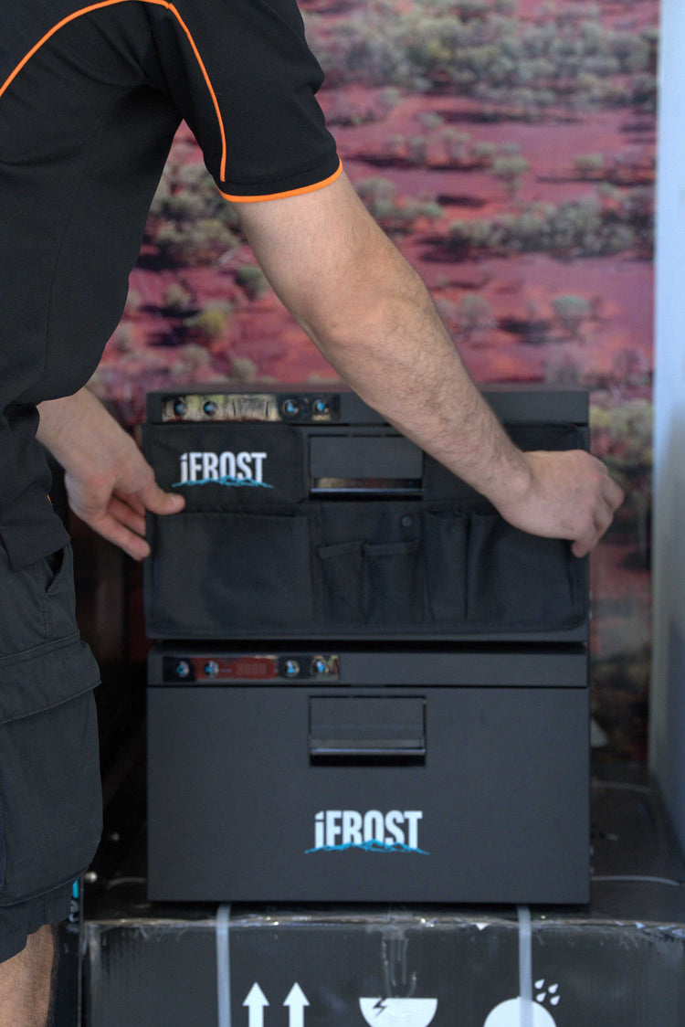 A person wearing a black shirt with orange trim is handling a black Jerost cooler or storage unit with multiple front compartments and visible Jerost branding.