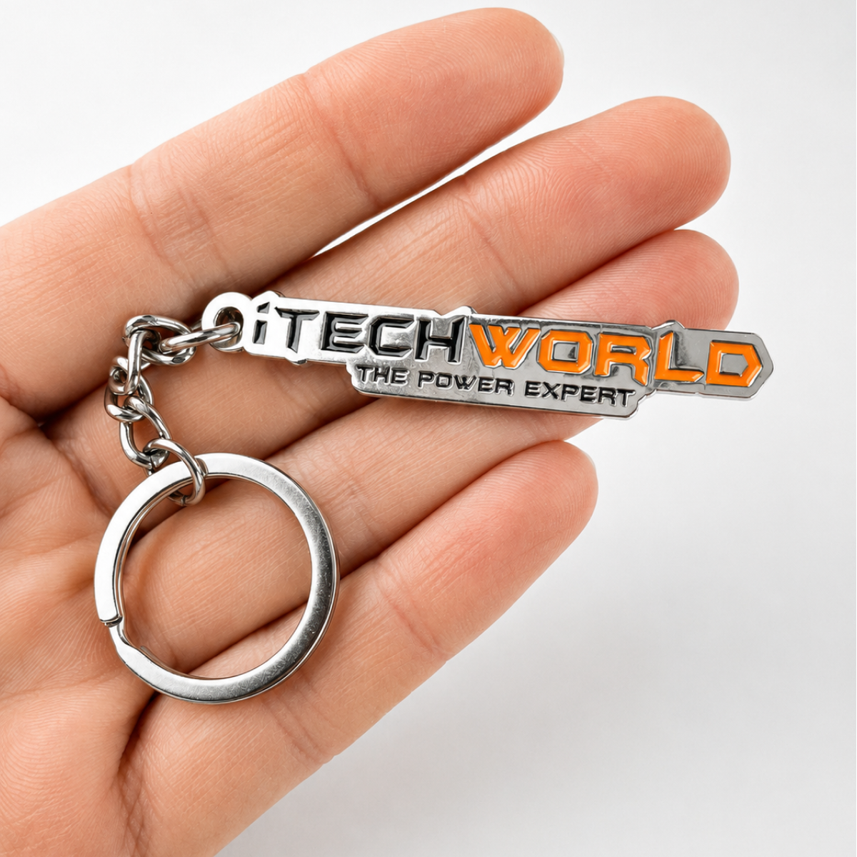 A hand holds an iTechworld iron keyring with laser-etched branding in black and orange, attached to a silver keyring.